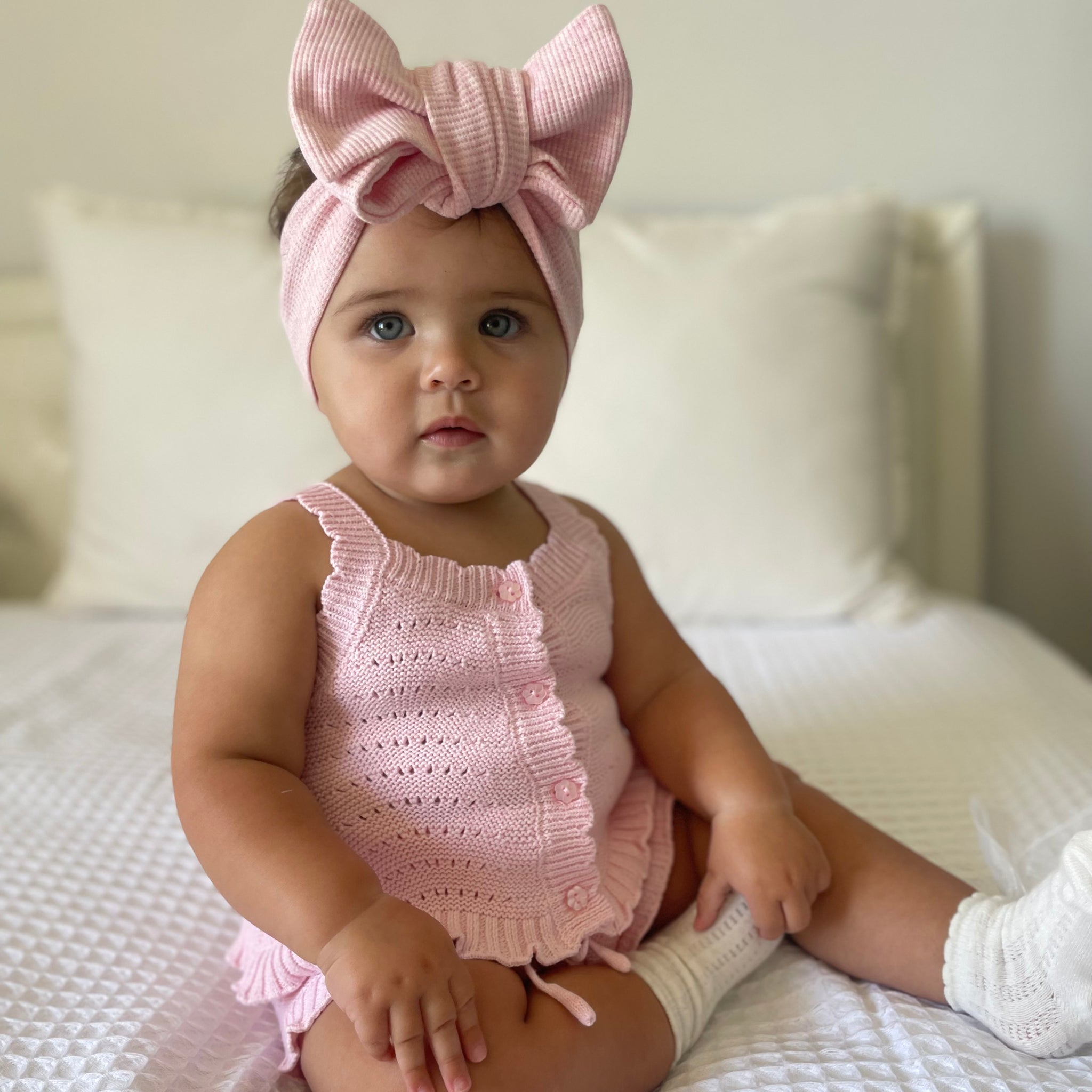 Baby in a florence lace pink knitted top and shorts sitting on soft bed