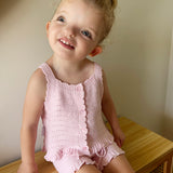 pink knitted short sleeve singlet top. eyelet wave pattern light weight frill on hem, Young girl 3 years old wearing top & shorts sitting on bench
