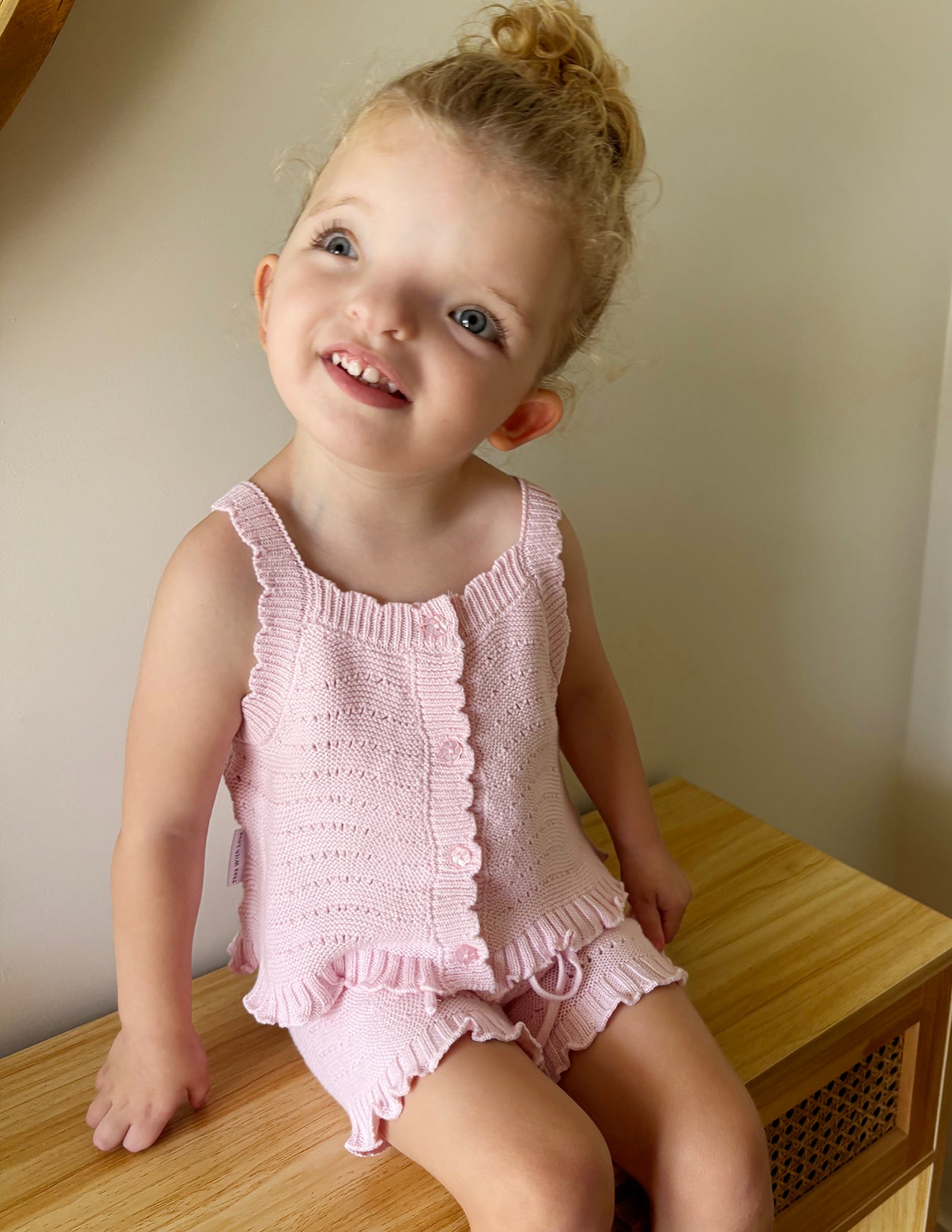 pink knitted short sleeve singlet top. eyelet wave pattern light weight frill on hem, Young girl 3 years old wearing top & shorts sitting on bench