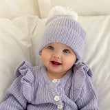 baby girl wearing lavender pom pom beanie and frilly matching romper