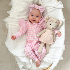 baby dressed in pink gingham frilly onesie with matching one size bow laying on white blanket