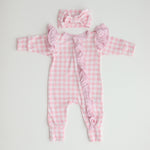 A pink gingham frilly onesie with long sleeves and a matching gingham bow, laid flat on a white background.