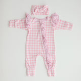 A pink gingham frilly onesie with long sleeves and a matching gingham bow, laid flat on a white background.