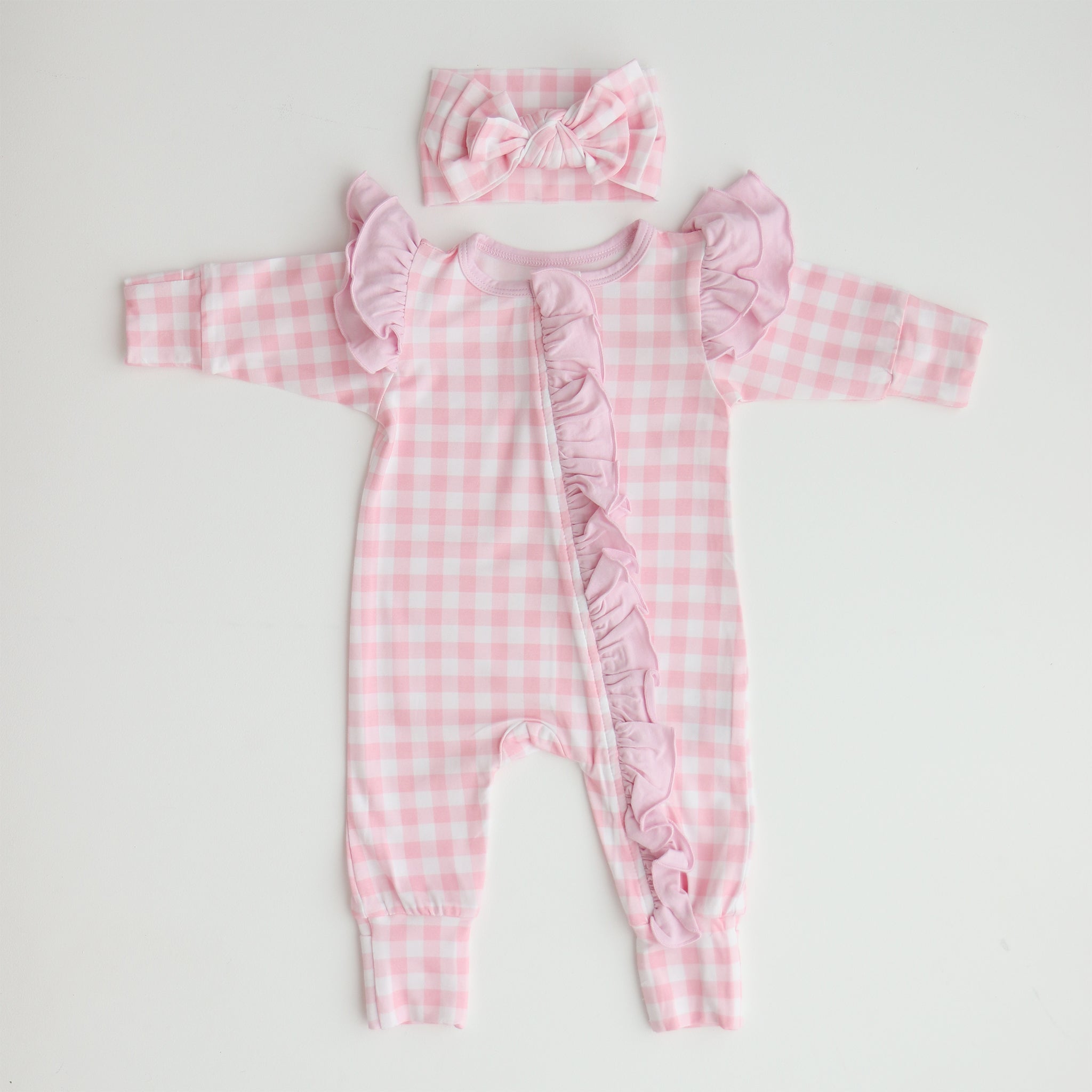 A pink gingham frilly onesie with long sleeves and a matching gingham bow, laid flat on a white background.