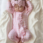 baby dressed in pink gingham frilly onesie with matching one size bow laying on white blanket
