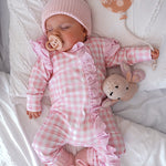 baby dressed in pink gingham frilly onesie with matching one size bow laying on white blanket