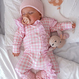 baby dressed in pink gingham frilly onesie with matching one size bow laying on white blanket