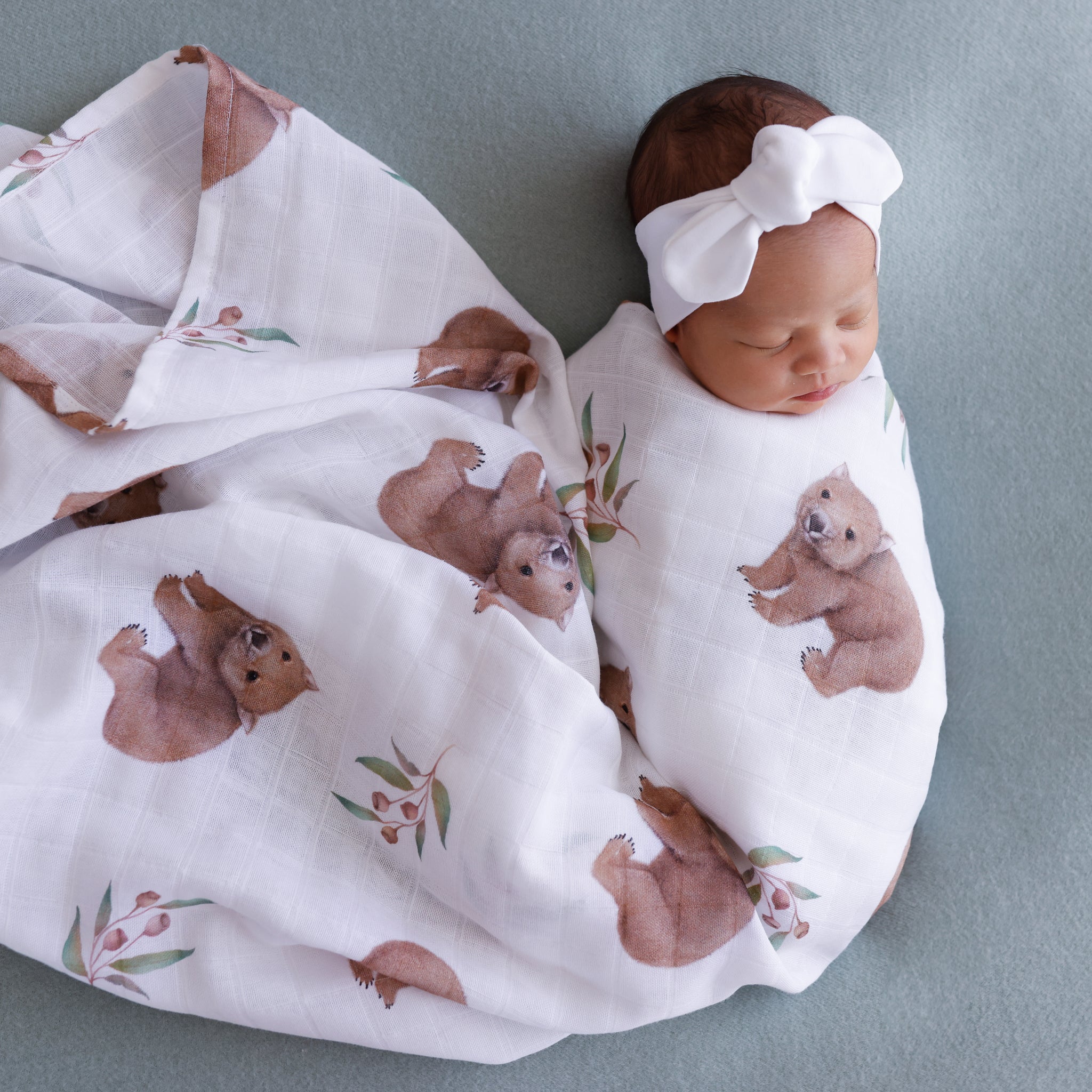 wombat print on a gots certified organic muslin swaddle wrapped on a baby .Baby is also wearing a white Thea with Love topknot on her head