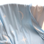 Light blue baby blanket with star and moon patterns on a cane bassinet.