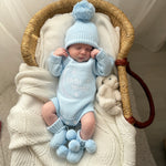 Newborn baby in a baby blue hello world outfit and beanie and booties with a teddy bear, lying in a woven basket.