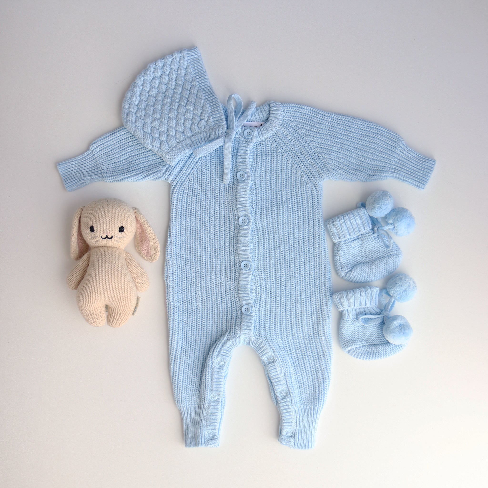 Blue knitted baby outfit with a plush toy on a light background