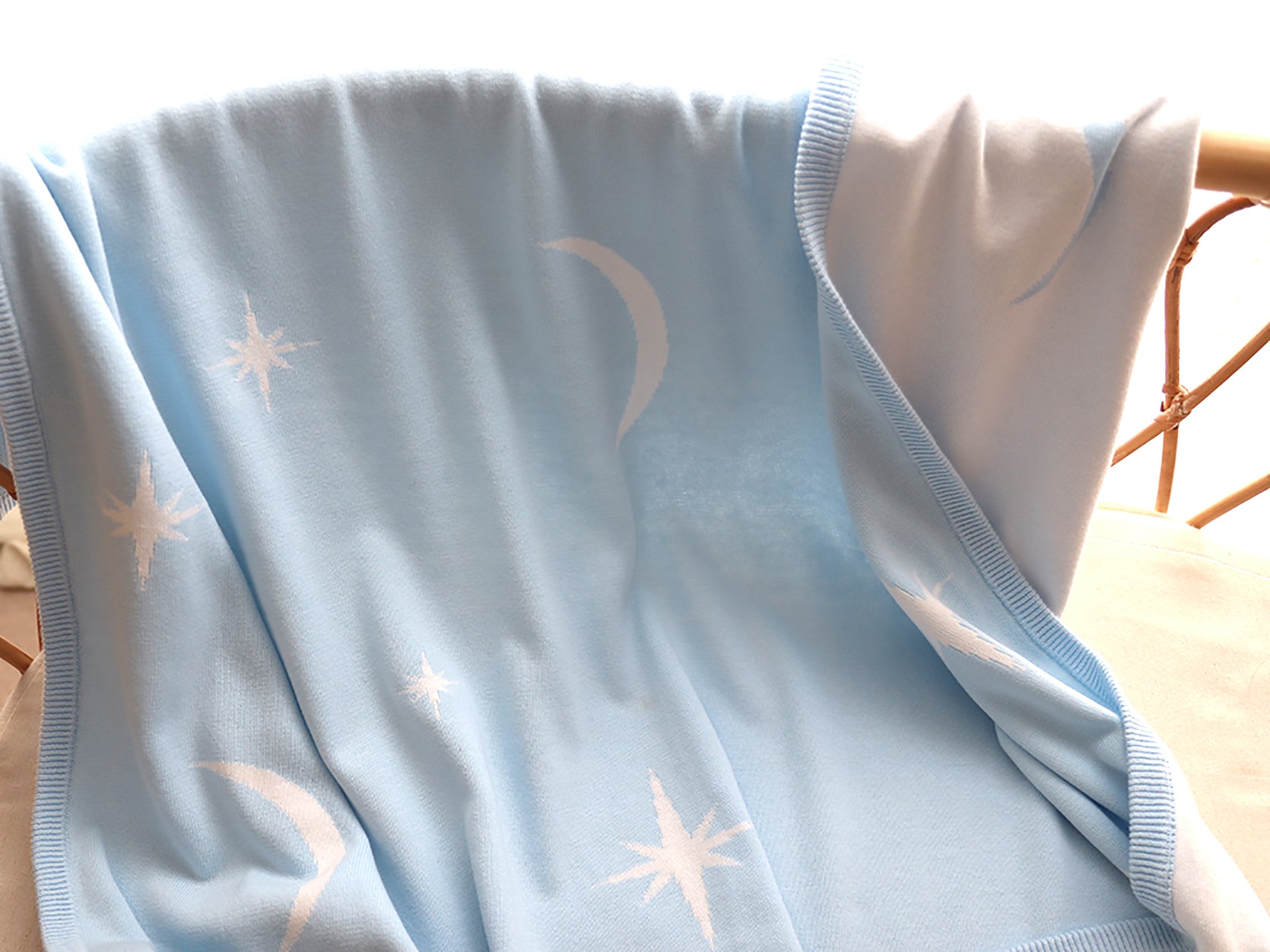 Light blue baby blanket with star and moon patterns on a cane bassinet.