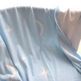 Light blue baby blanket with star and moon patterns on a cane bassinet.