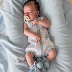 baby dressed in the coastal bubble romper laying on baby blue blanket wear baby blue booties and dummy in mouth