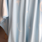 Baby blue blanket with star and moon patterns draped over cane bassinet.

