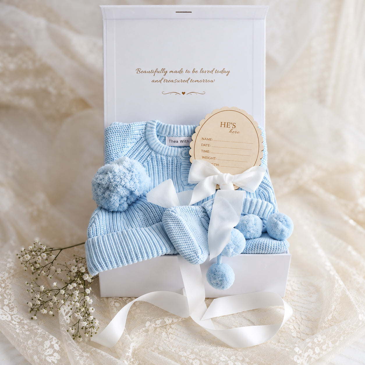 Baby gift box with baby blue knit romper, booties, beanie and He's Here disc with white ribbon
