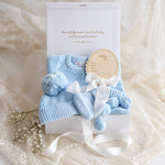 Baby gift box with baby blue knit romper, booties, beanie and He's Here disc with white ribbon