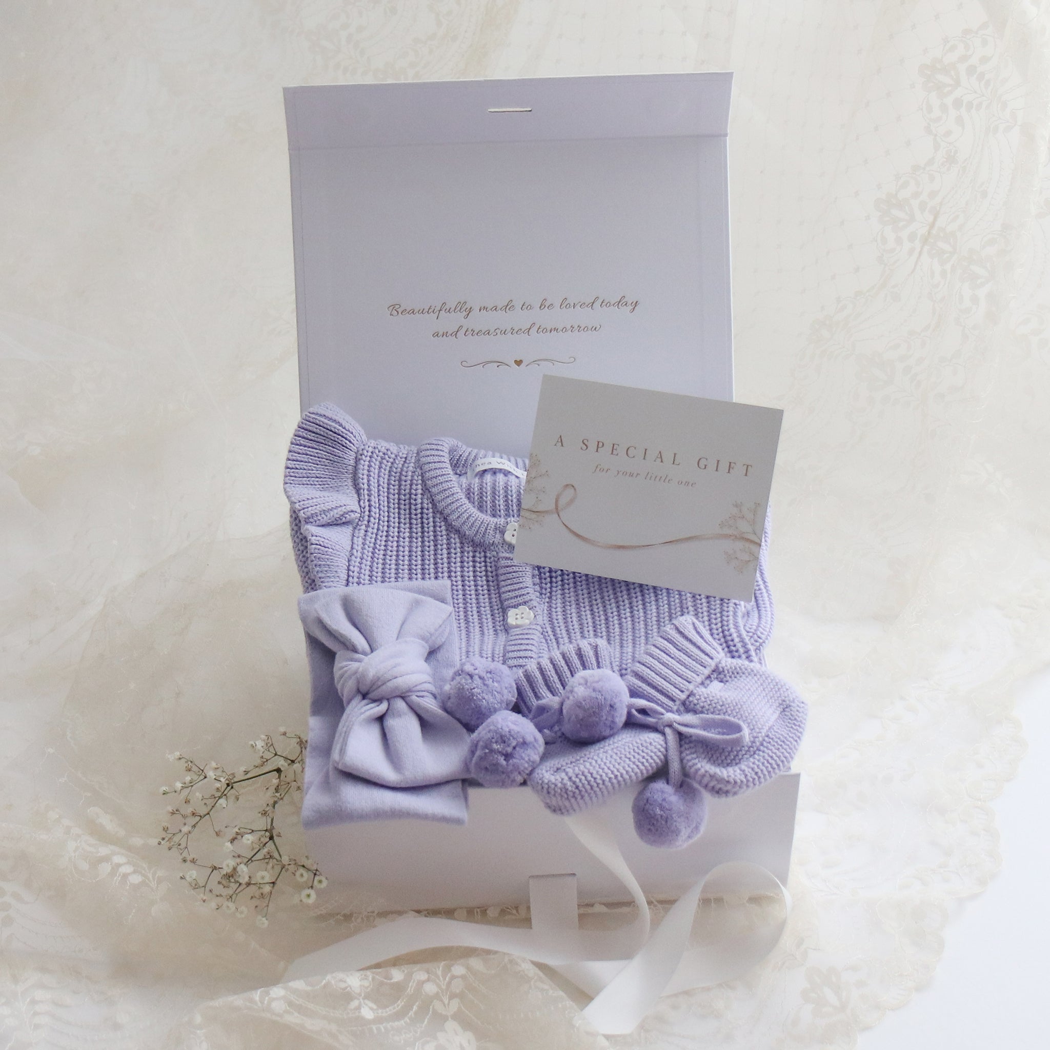 white gift box with lavender frill romper bow and pom pom booties on lace cloth card writing a "a special gift"