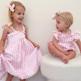 Two young girls in matching pink checkered dresses standing on a white surface.