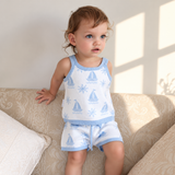 Toddler wearing Coastal Cotton Knitted Shorts and Singlet Top, light blue and white knit with sailboat and sun pattern, sitting on a beige sofa