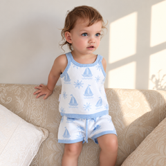 Toddler wearing Coastal Cotton Knitted Shorts and Singlet Top, light blue and white knit with sailboat and sun pattern, sitting on a beige sofa