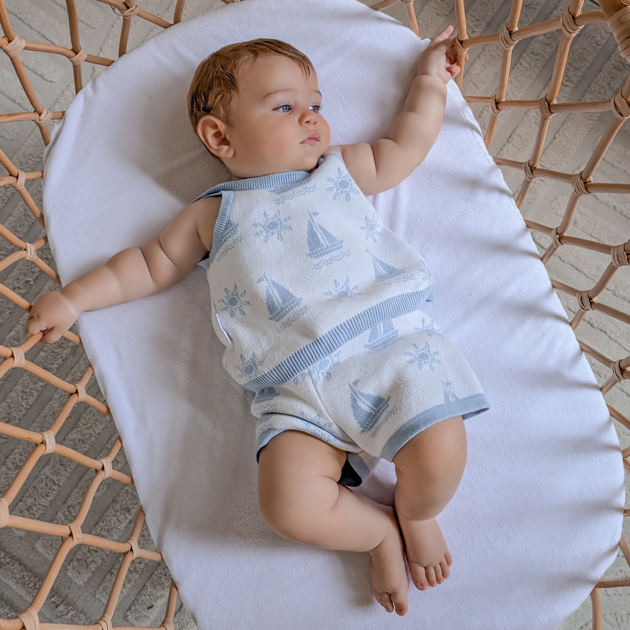 BABY WEARING KNITTED SINGLET TOP AND MATCHING SHORTS LYING IN A BASSINET