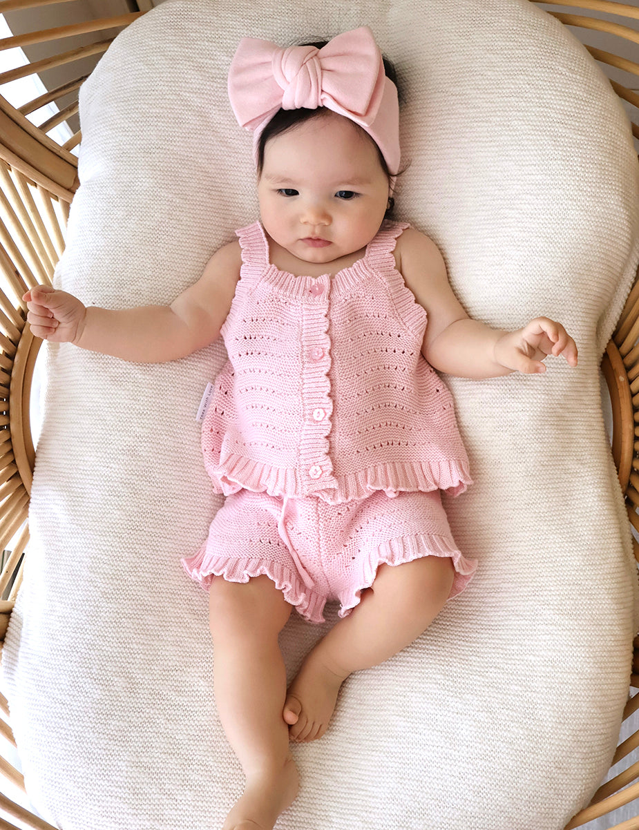 Baby in pink florence lace top and shorts with a matching bow headband lying in bassinet