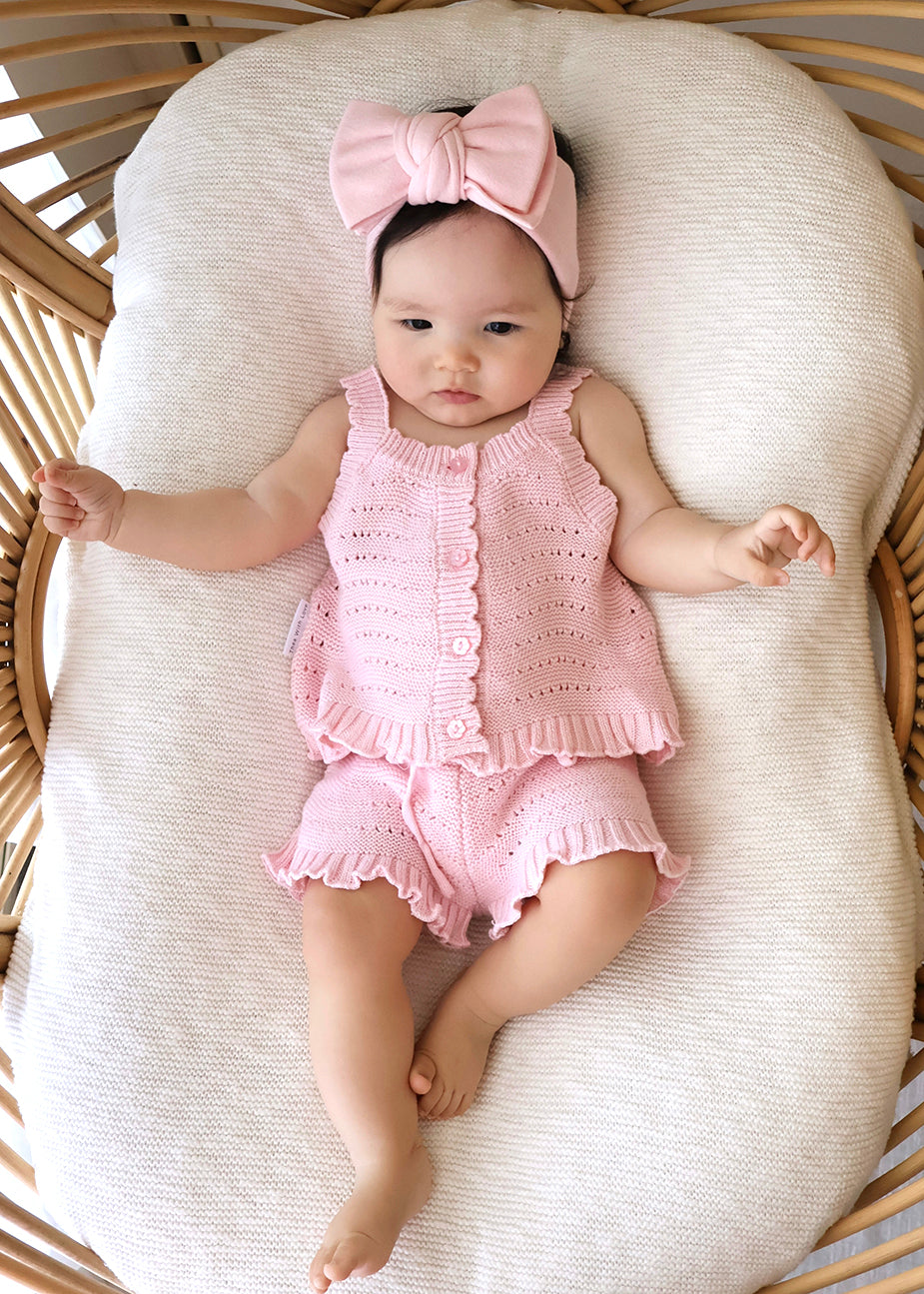 Baby in pink florence lace top and shorts with a matching bow headband lying in bassinet