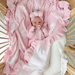 Baby in pink outfit with matching blanket in a crib