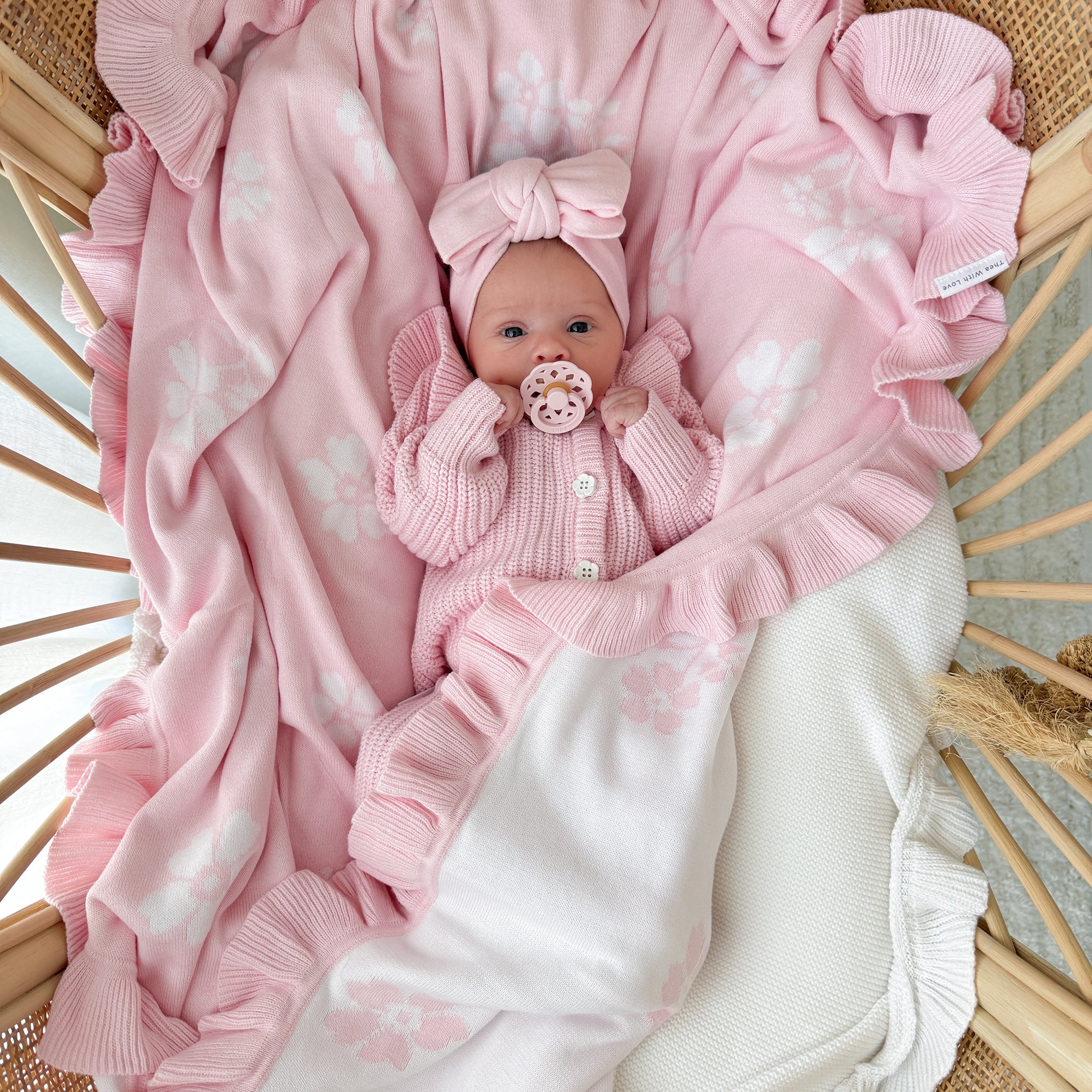 Baby in pink outfit with matching blanket in a crib