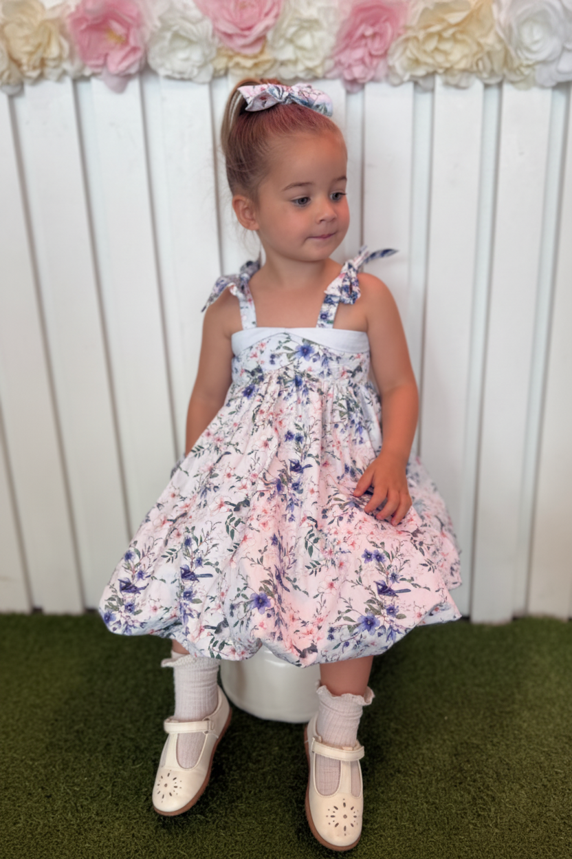 Young girl in a floral dress sitting on a stool with a white background
