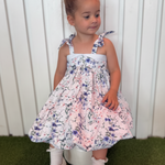 Young girl in a floral dress sitting on a stool with a white background