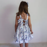 Young girl wearing a floral dress with a cutout back design against a plain background