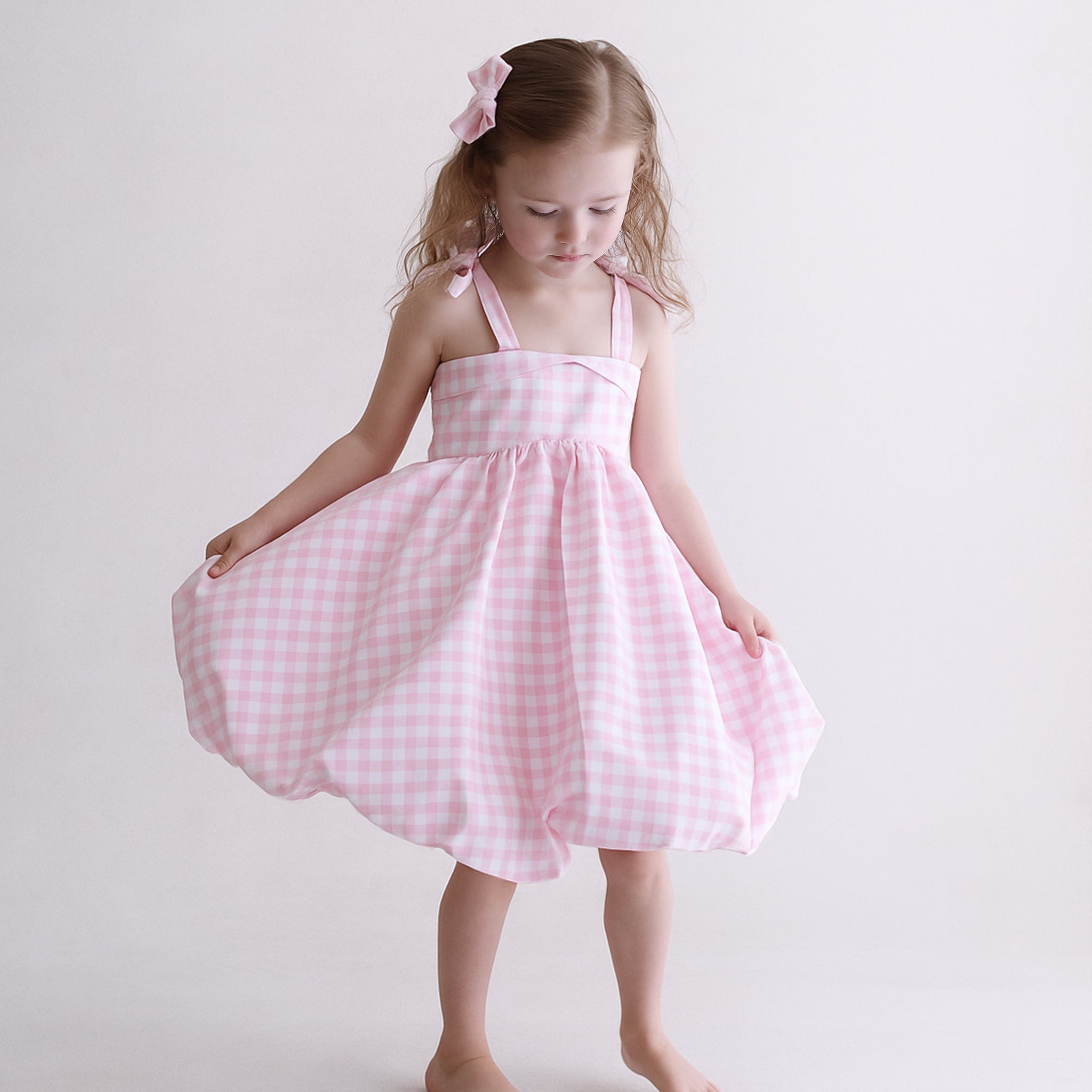 Young girl wearing a pink checkered dress against a white background