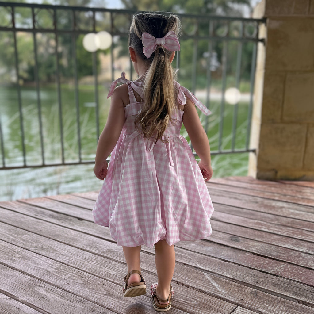 Child in a pink gingham dress standing on a wooden deck with a lake view.