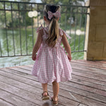 Child in a pink gingham dress standing on a wooden deck with a lake view.