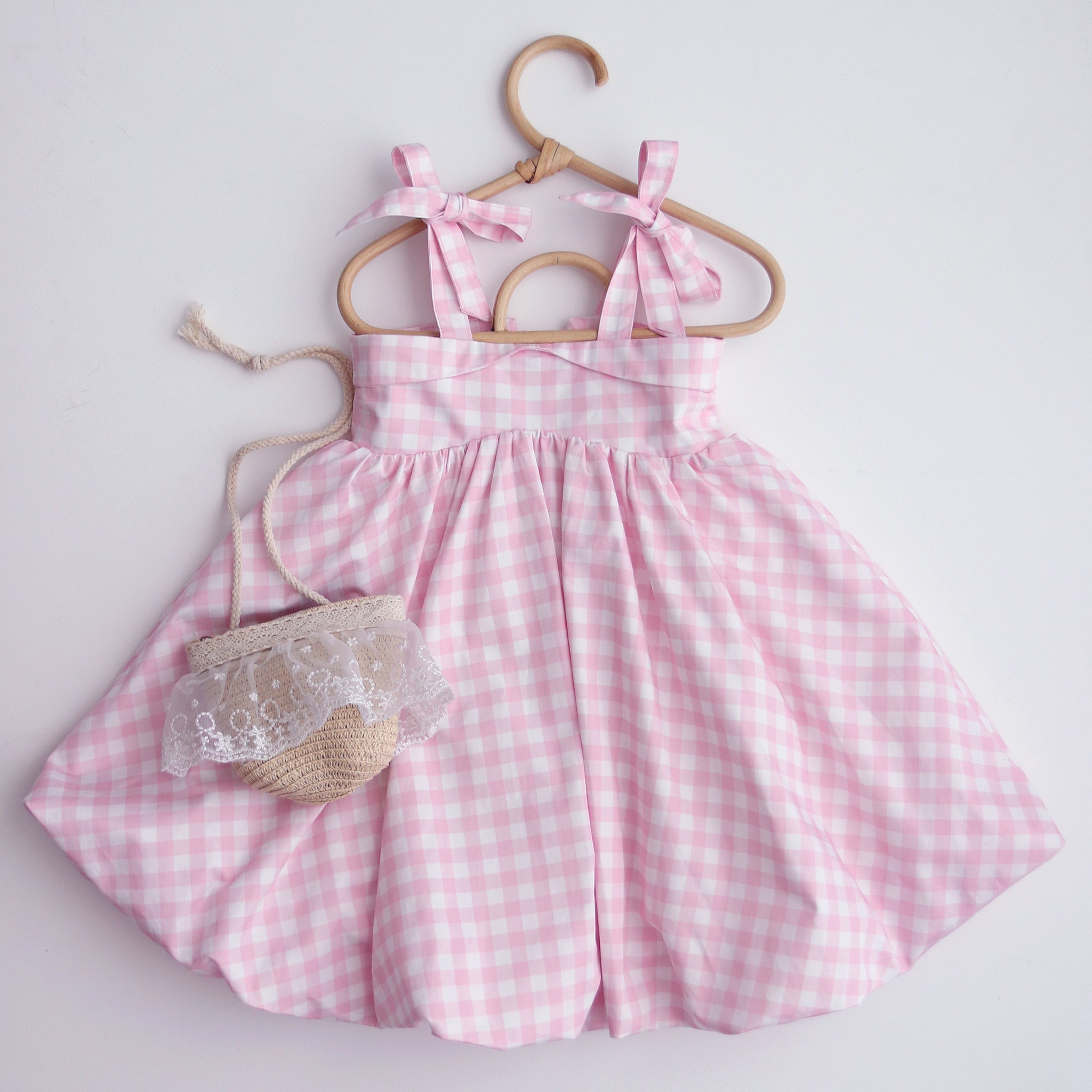 Pink checkered dress with a matching bag on a hanger against a light background