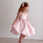 Young girl wearing a pink checkered dress against a plain white background