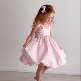 Young girl wearing a pink checkered dress against a plain white background