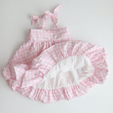 Pink and white checkered baby dress with ruffled details on a light gray background