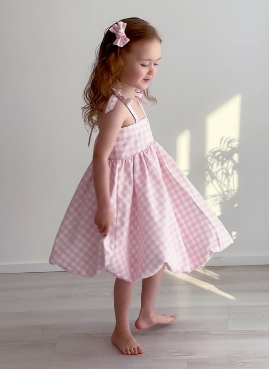Young girl wearing a pink checkered dress standing in a softly lit room.