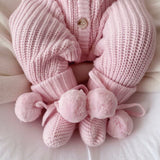baby wearing pink booties with pom poms