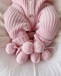 baby wearing pink booties with pom poms