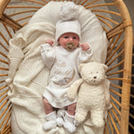 


Newborn baby in a white outfit with 'Hello World' text, surrounded by soft textures and a teddy bear in a wicker crib.