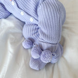 lavender knitted baby outfit with pom-pom booties details on a light background