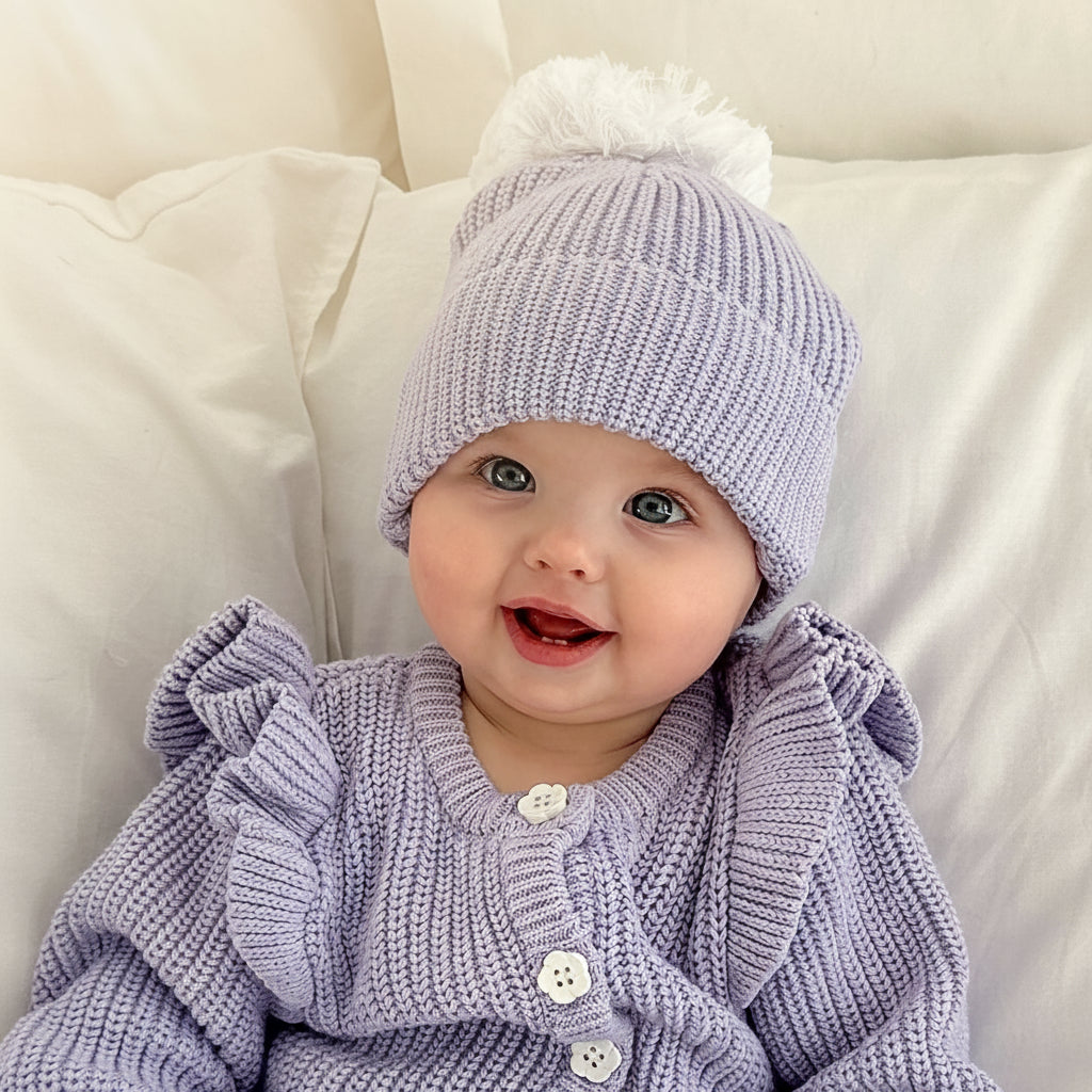 baby girl wearing lavender pom pom beanie and frilly matching romper