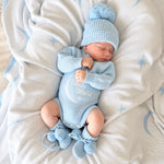 A sleeping newborn baby wearing a light blue knit onesie with 'Hello World' and a crescent moon design, along with a matching blue pom-pom beanie and booties, lying on a white blanket with blue star and moon patterns.

Details