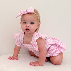 Baby in a pink outfit with a bow sitting on a white surface