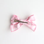 Pink bow hair clip on a white background showing back of the bow with the clip