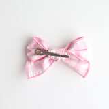Pink bow hair clip on a white background showing back of the bow with the clip